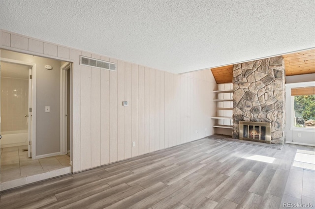 2453 S Xanadu Way Unit C, Aurora, CO 80014 - unfurnished living room featuring wood finished floors, a stone fireplace, a textured ceiling, and wood walls