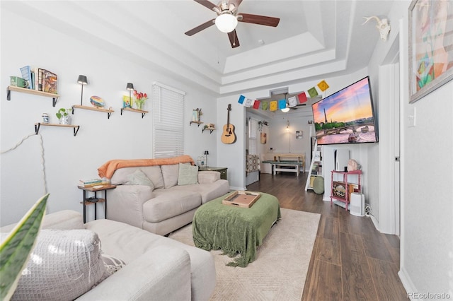 living area featuring baseboards, ceiling fan, a tray ceiling, and dark wood-type flooring