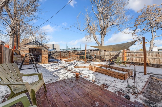 snow covered patio with an outbuilding, a deck, a fenced backyard, a vegetable garden, and a storage unit