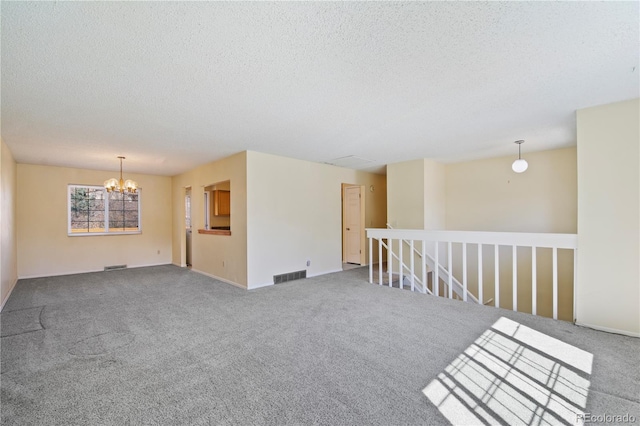 carpeted empty room with a chandelier, a textured ceiling, and visible vents