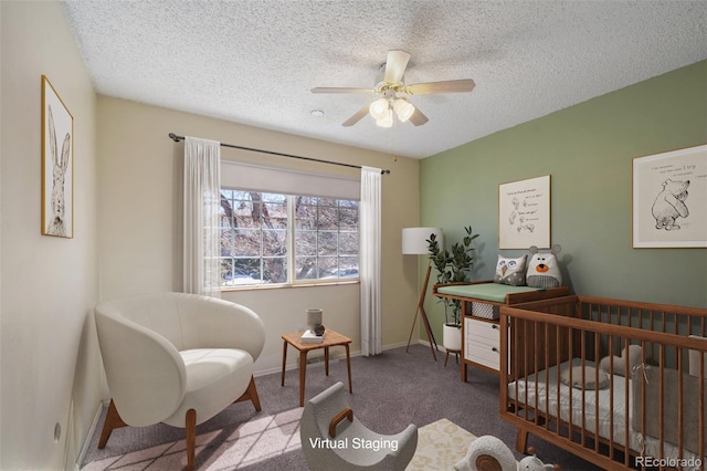 carpeted bedroom with a nursery area, ceiling fan, baseboards, and a textured ceiling