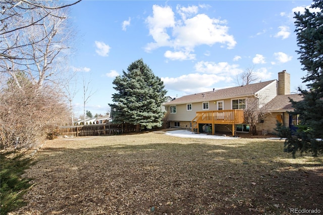 rear view of house featuring a deck, a patio, fence, a lawn, and a chimney