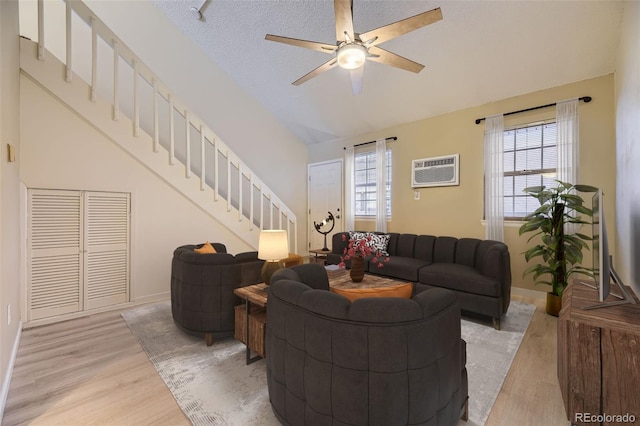 living room with an AC wall unit, a textured ceiling, a wealth of natural light, and light hardwood / wood-style flooring