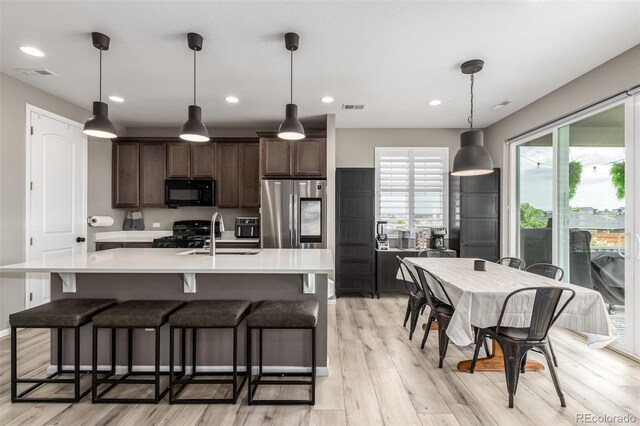 kitchen featuring black appliances, an island with sink, sink, dark brown cabinetry, and light wood-type flooring