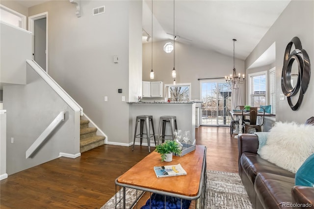 living room with stairway, wood finished floors, visible vents, high vaulted ceiling, and a chandelier