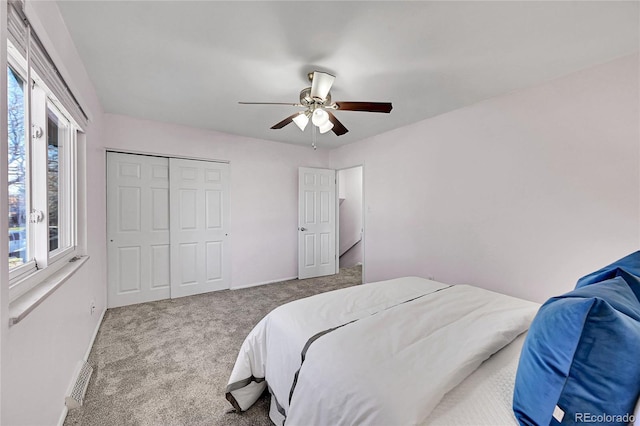 bedroom with a closet, light colored carpet, multiple windows, and ceiling fan