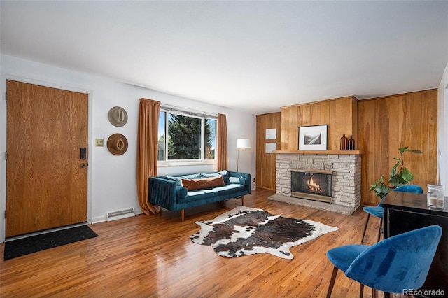 living area featuring a stone fireplace, wood walls, wood finished floors, and visible vents