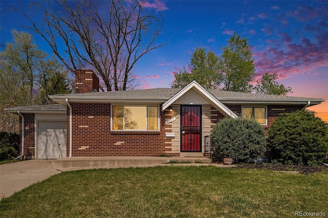 view of front of home with a garage, a chimney, brick siding, a lawn, and driveway