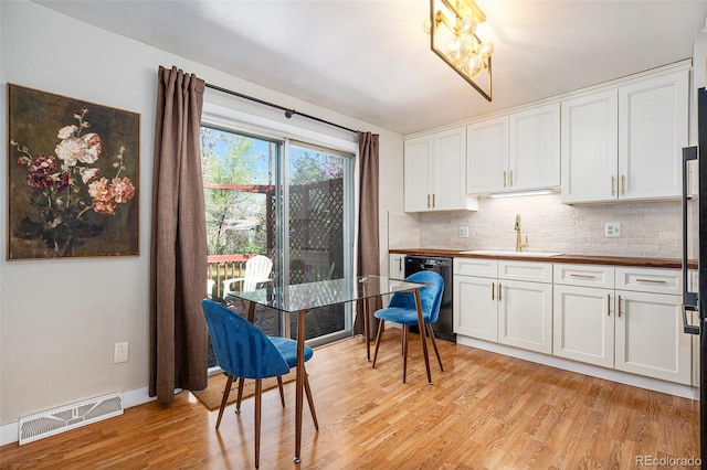 kitchen with visible vents, black dishwasher, tasteful backsplash, a sink, and light wood finished floors