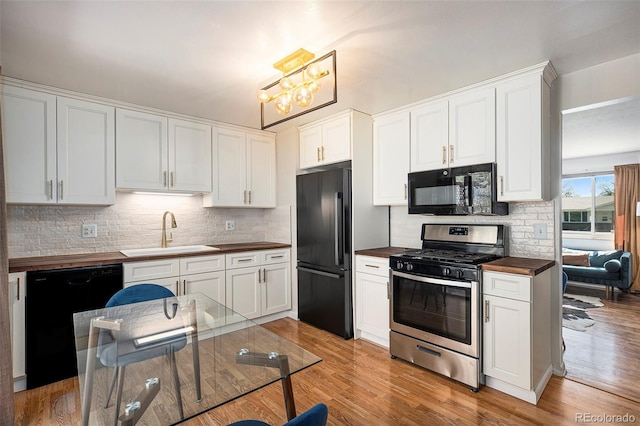 kitchen featuring tasteful backsplash, a sink, butcher block countertops, light wood-type flooring, and black appliances