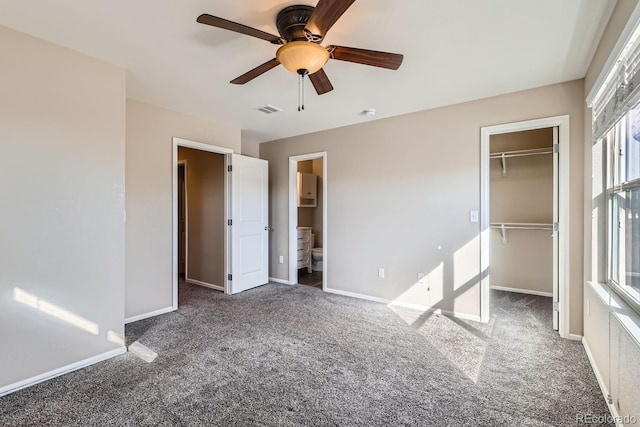 unfurnished bedroom featuring connected bathroom, a spacious closet, dark carpet, a closet, and ceiling fan