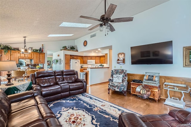 living room featuring wood walls, ceiling fan with notable chandelier, light hardwood / wood-style flooring, vaulted ceiling, and a textured ceiling