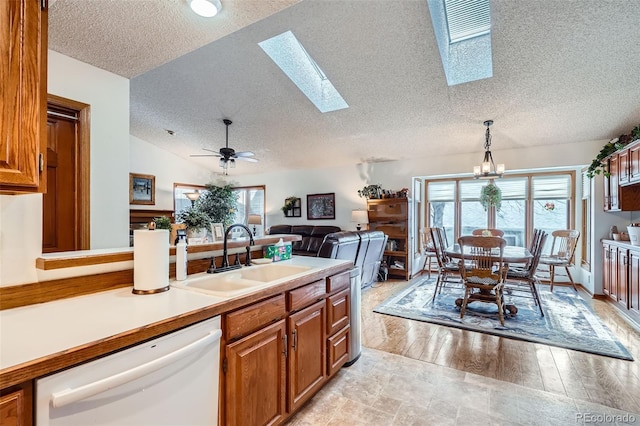 kitchen featuring dishwasher, ceiling fan with notable chandelier, sink, vaulted ceiling with skylight, and decorative light fixtures