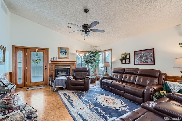 living room with lofted ceiling, ceiling fan, a textured ceiling, and light wood-type flooring