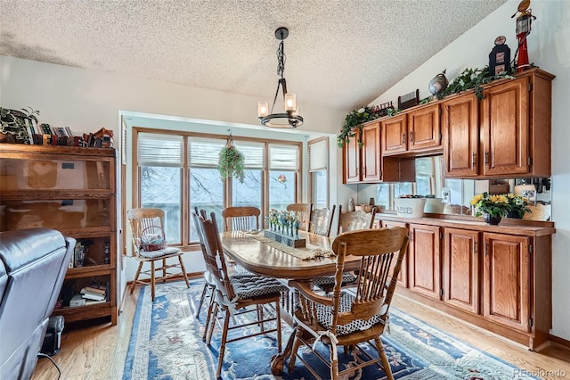 dining space featuring a chandelier, a textured ceiling, vaulted ceiling, and light hardwood / wood-style flooring