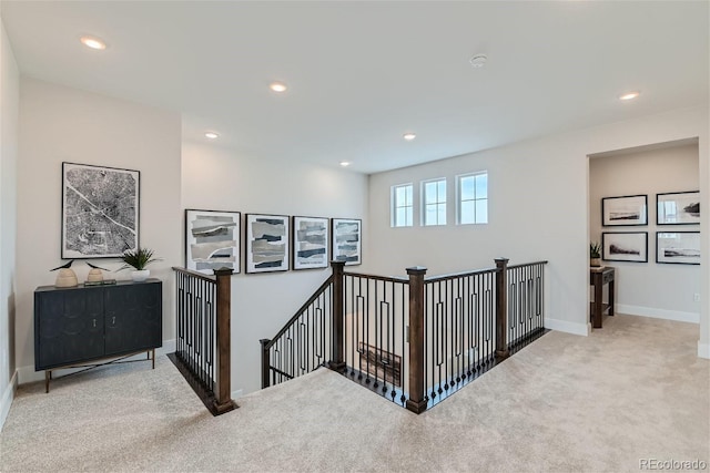 hall featuring light carpet, recessed lighting, baseboards, and an upstairs landing