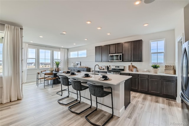 kitchen with a kitchen island with sink, a healthy amount of sunlight, light countertops, appliances with stainless steel finishes, and backsplash