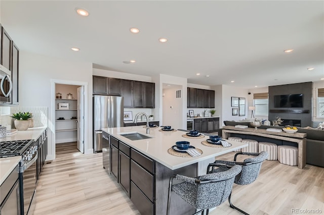 kitchen featuring a center island with sink, stainless steel appliances, light countertops, open floor plan, and a sink