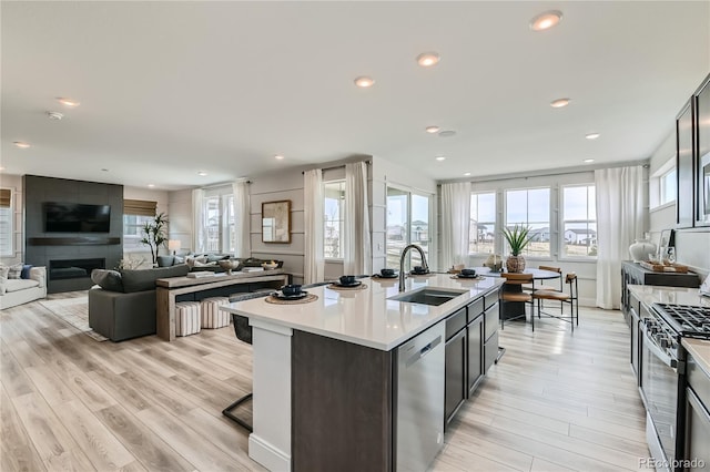 kitchen featuring light countertops, appliances with stainless steel finishes, open floor plan, a sink, and an island with sink