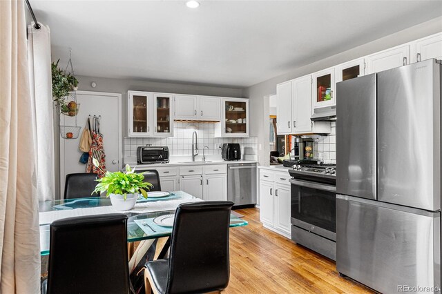 kitchen featuring appliances with stainless steel finishes, white cabinets, sink, tasteful backsplash, and light hardwood / wood-style floors