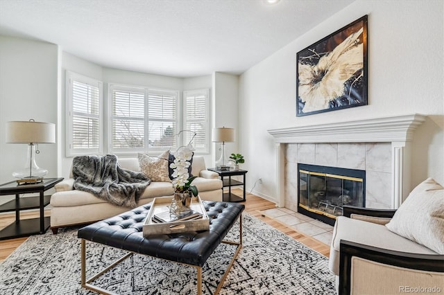 living area with a tile fireplace, baseboards, and light wood finished floors