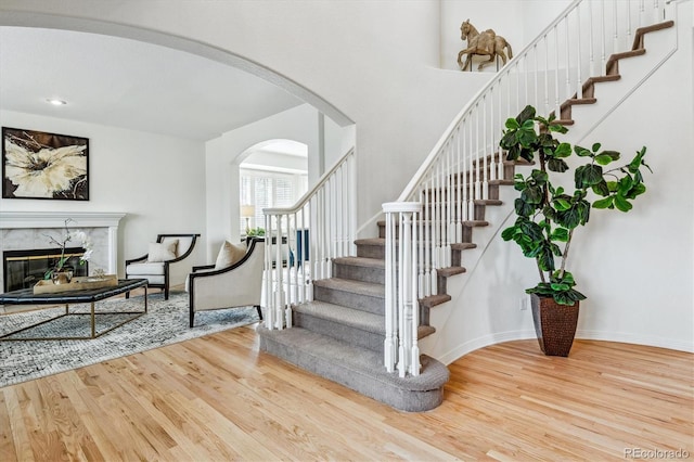 staircase featuring baseboards, arched walkways, a premium fireplace, wood finished floors, and a high ceiling