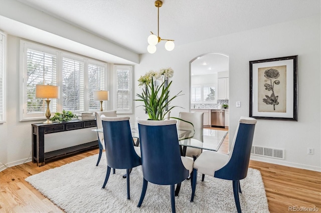 dining area featuring arched walkways, light wood-type flooring, visible vents, and baseboards