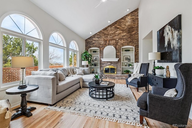 living room featuring high vaulted ceiling, a brick fireplace, and wood finished floors