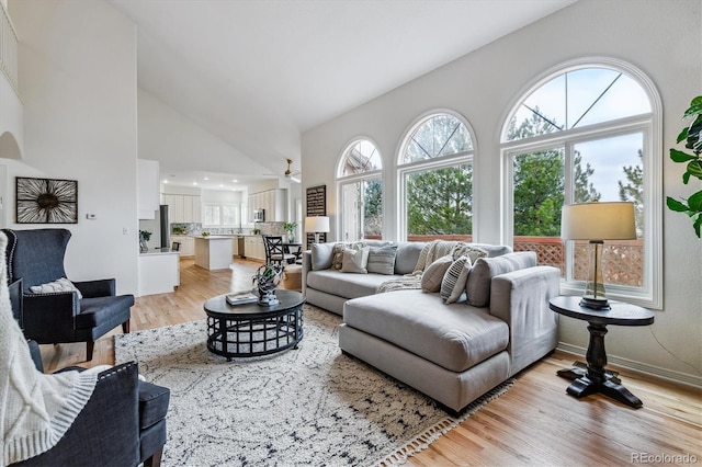 living room featuring high vaulted ceiling, light wood finished floors, and baseboards