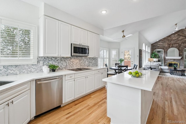 kitchen with vaulted ceiling, stainless steel appliances, a large fireplace, and white cabinetry