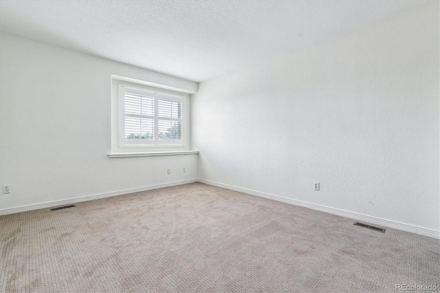 spare room with a textured ceiling, carpet, visible vents, and baseboards