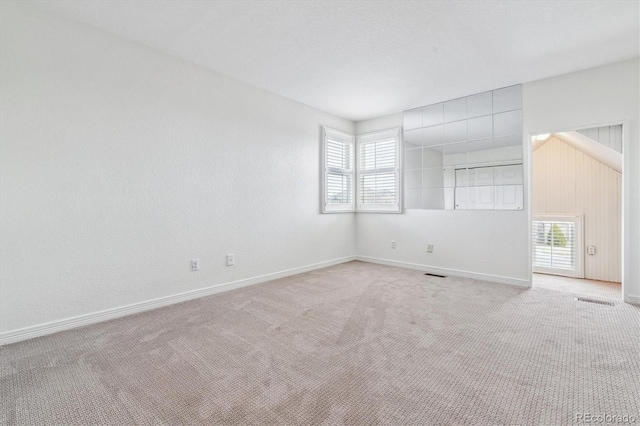 empty room with baseboards, a healthy amount of sunlight, visible vents, and light colored carpet