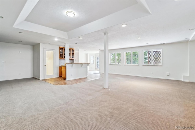 unfurnished living room with a tray ceiling, light carpet, baseboards, and recessed lighting