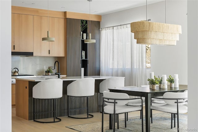 kitchen featuring tasteful backsplash, decorative light fixtures, light wood-type flooring, and light brown cabinets