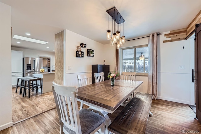 dining area with a notable chandelier, a skylight, and light wood-type flooring