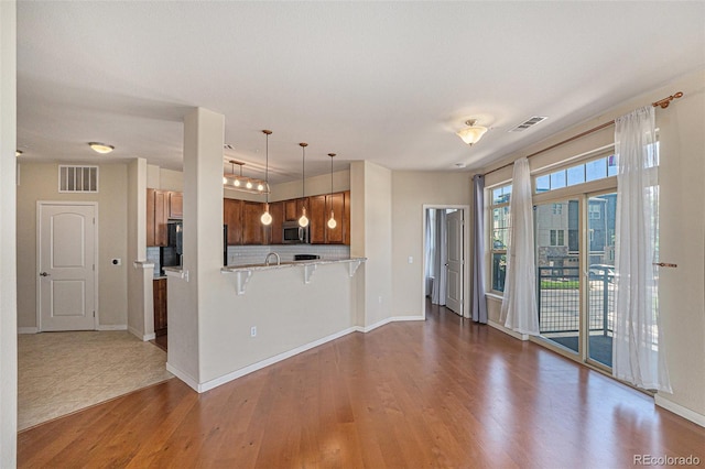 13456 Via Varra Unit 140, Broomfield, CO 80020 - kitchen featuring stainless steel microwave, wood finished floors, a kitchen bar, brown cabinets, and light countertops
