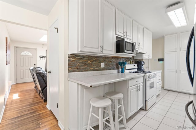 3397 W Tanforan Dr, Englewood, CO 80110 - kitchen with white gas range, stainless steel microwave, light countertops, decorative backsplash, and white cabinetry
