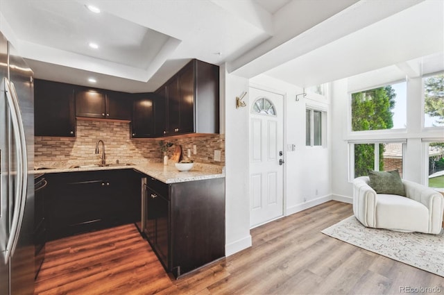 kitchen with dark brown cabinetry, sink, light hardwood / wood-style flooring, stainless steel fridge, and backsplash