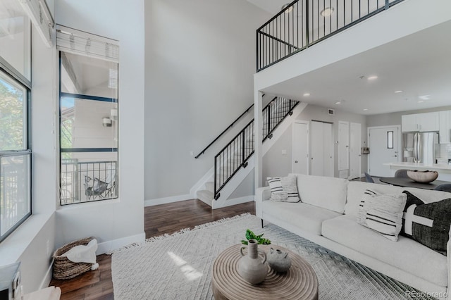 living area with recessed lighting, wood finished floors, a towering ceiling, baseboards, and stairway