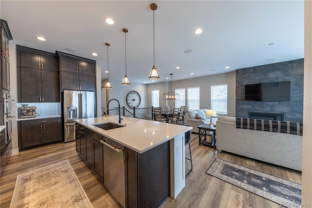 kitchen with a tile fireplace, pendant lighting, sink, a kitchen island with sink, and stainless steel appliances