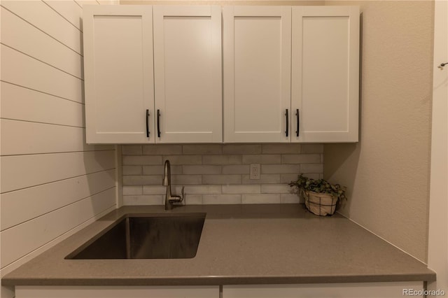 kitchen with wood walls, white cabinetry, backsplash, and sink