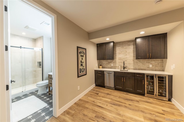 bar featuring dark brown cabinets, stainless steel dishwasher, light hardwood / wood-style flooring, and sink