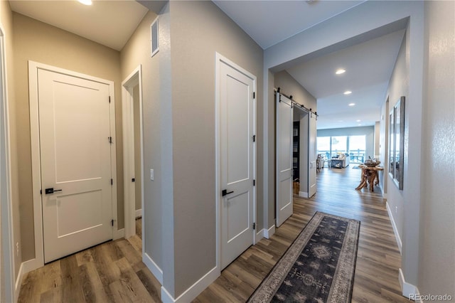 corridor featuring wood finished floors, baseboards, and a barn door