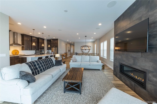 living room with a tile fireplace, light wood-style flooring, recessed lighting, baseboards, and an inviting chandelier