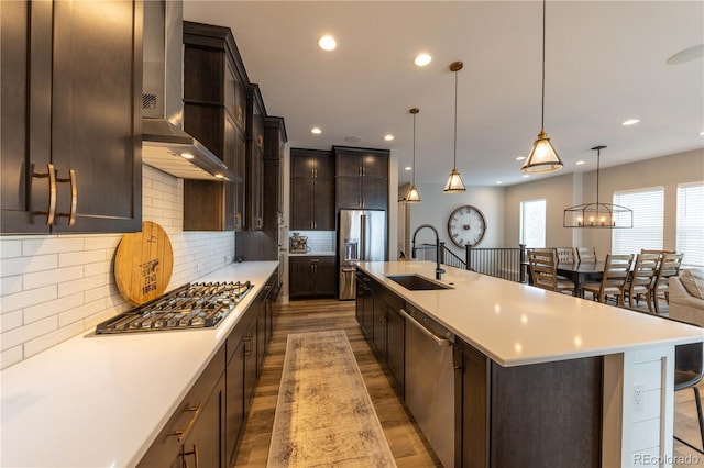 kitchen featuring stainless steel appliances, light countertops, light wood-style flooring, a sink, and wall chimney exhaust hood