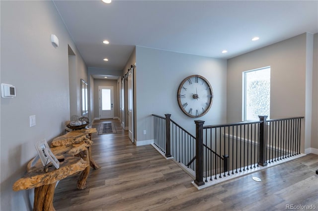hall featuring a barn door, recessed lighting, wood finished floors, and baseboards
