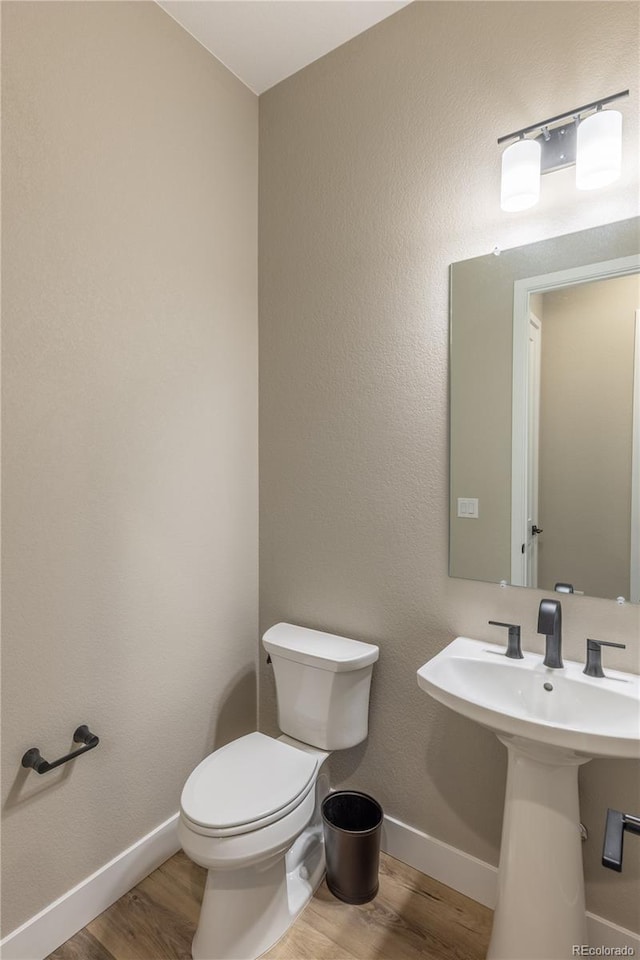 half bathroom featuring baseboards, toilet, and wood finished floors