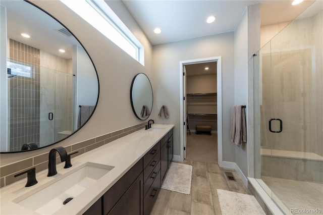 bathroom with a spacious closet, a stall shower, a sink, and visible vents