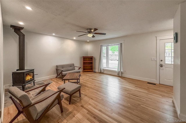 117 Sandler Dr, Lafayette, CO 80026 - living area with a wood stove, light wood finished floors, a textured ceiling, a ceiling fan, and baseboards