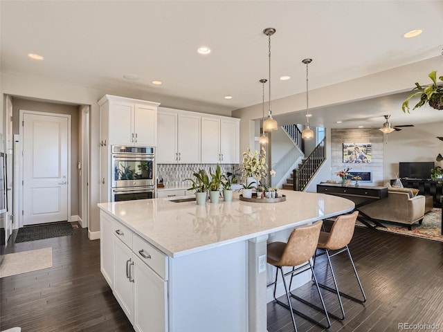 11096 Endeavor Dr, Parker, CO 80134 - kitchen with stainless steel double oven, open floor plan, a ceiling fan, white cabinets, and decorative backsplash